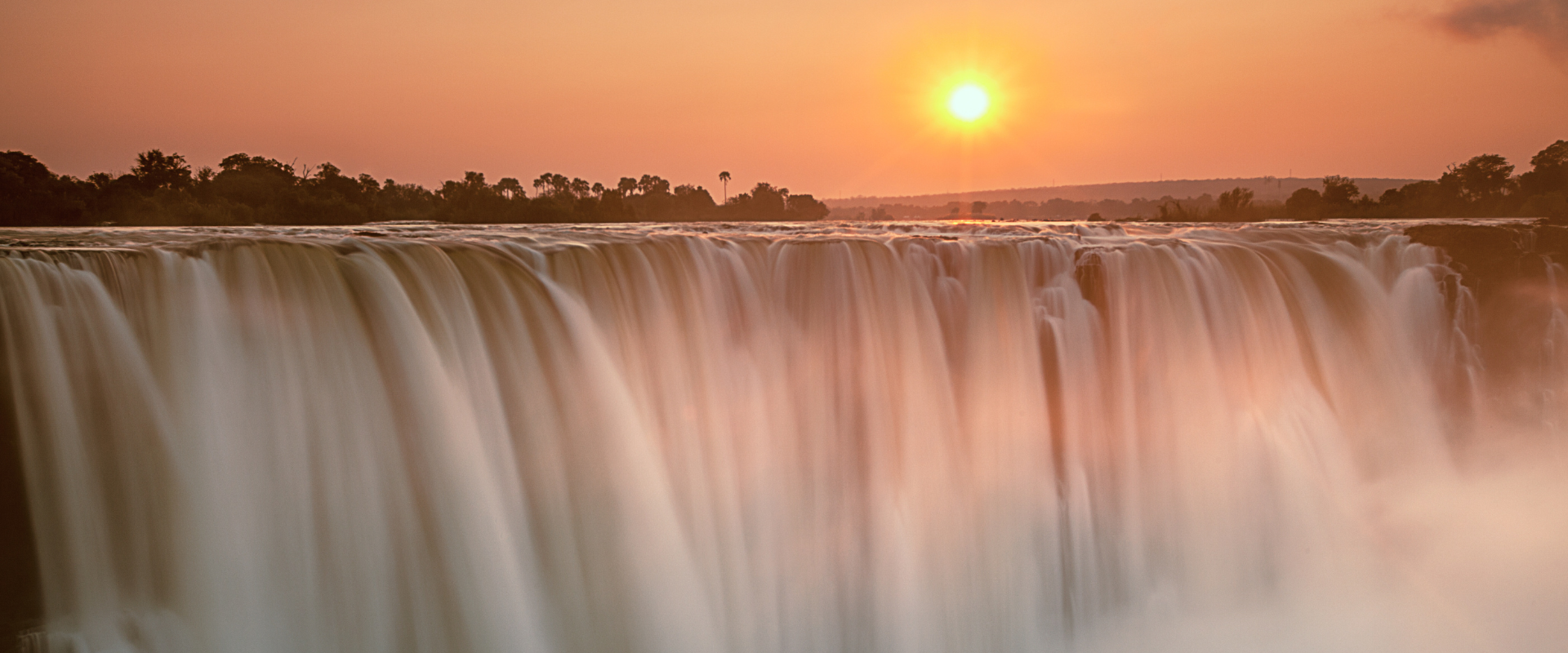 Victoria Falls under a pink sun and sky